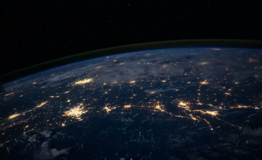 The darkened surface of the Earth at night, as seen from space, with lit-up cities visible.