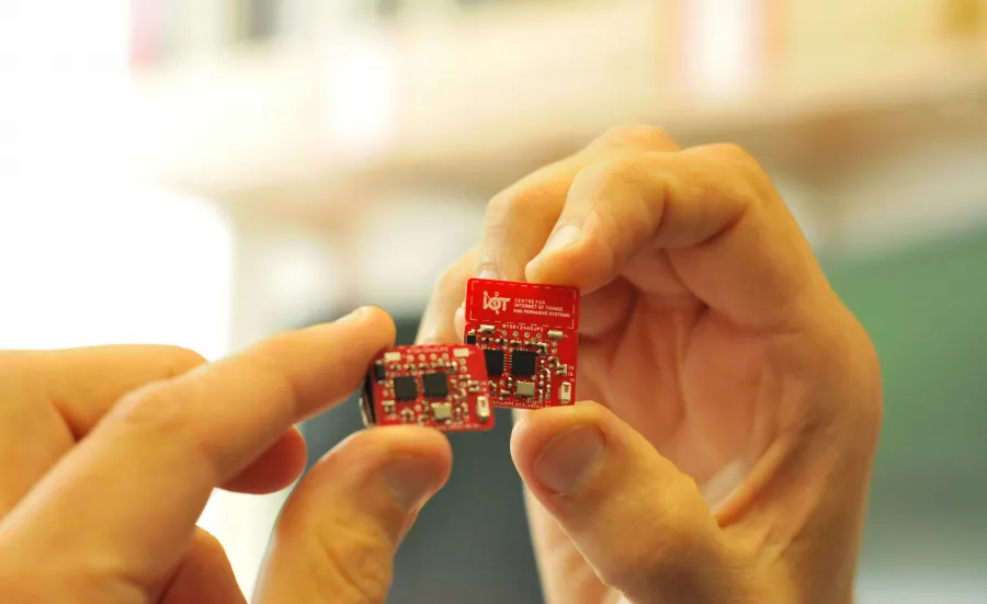 Hand holding a red internet of things circuit board created by the Centre for IoT and Pervasive Systems. 