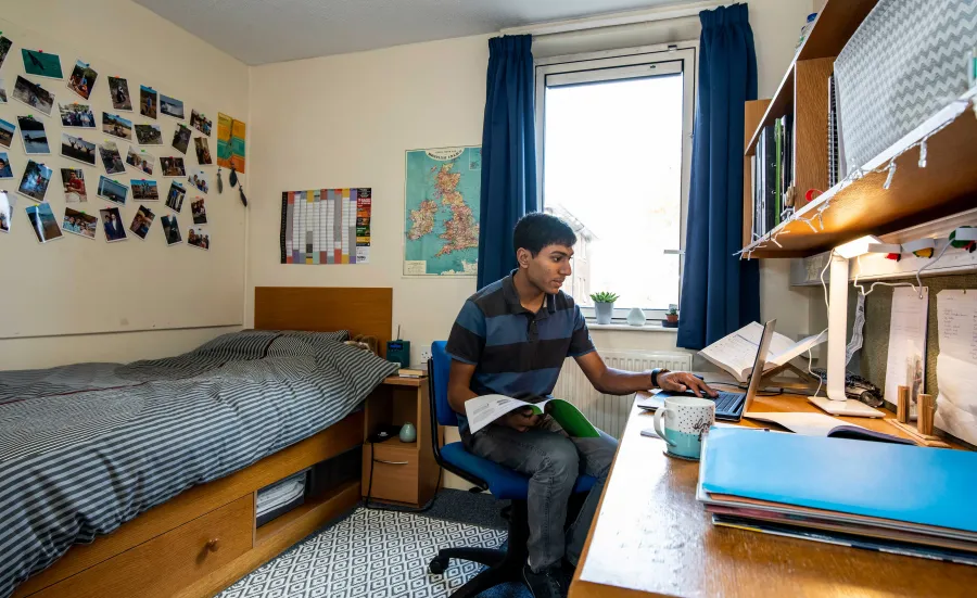 Student sat working at desk in bright, modern bedroom.