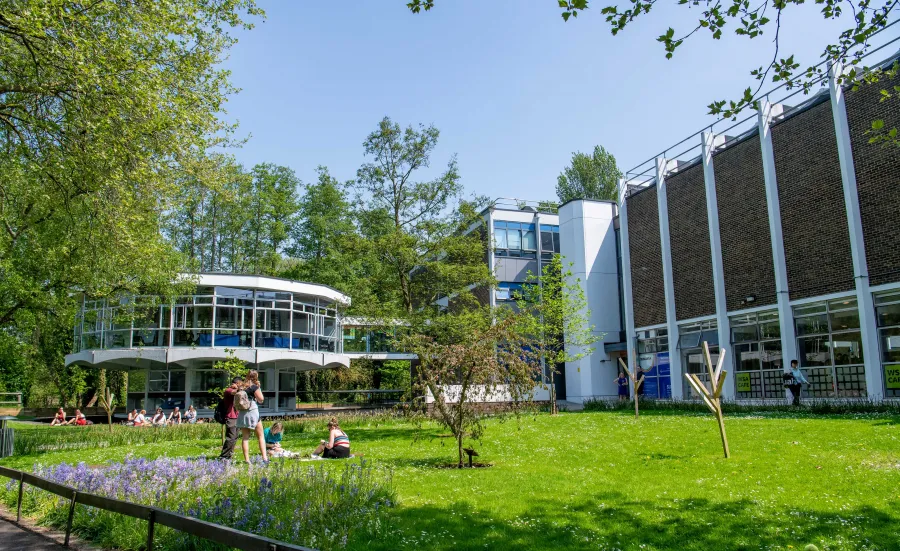 Modern looking campus building with, students relaxing on a grassy area in the foreground.