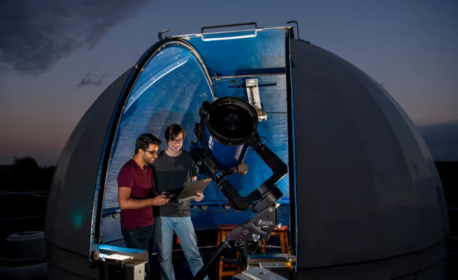 Astronomy students studying data in the shadow of a telescope and rooftop observatory dome.