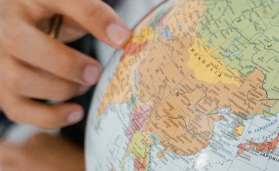 The hand of a young person points to a country on a globe model