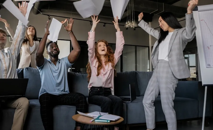 A diverse group of business people throw sheets of paper in the air in a celebratory fashion