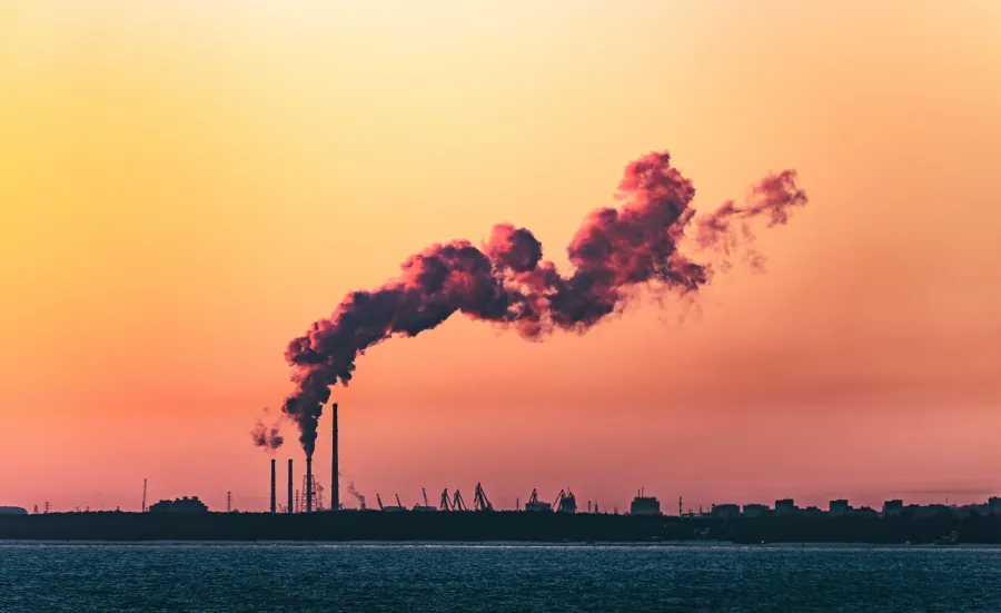 A shot of an industrial shoreline silhouetted at sunset, with smoke from a refinery curling into the sky.