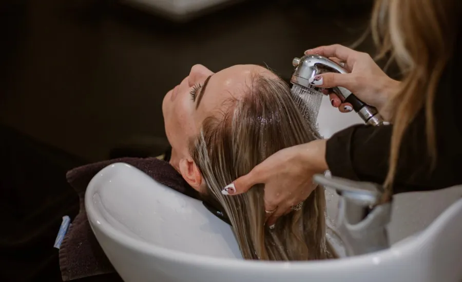 A hairdresser washes a client's hair at a basin