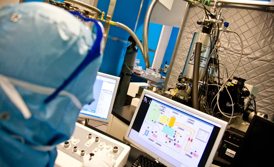 A researcher analysing a complex electrical circuit on a monitor in a cleanroom.