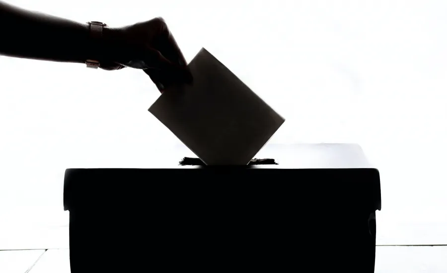 A silhouette of somebody's hand placing their vote into the polling booth box
