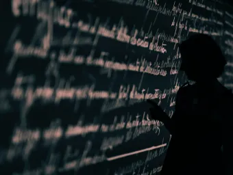 Stock image of a researcher's silhouette set against a wall projection of written language.