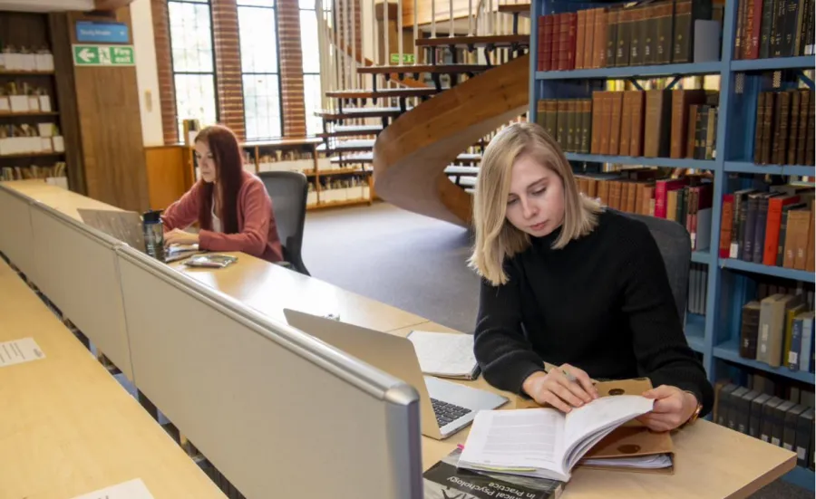 Students studying in Hartley Library with bookshelves in the background